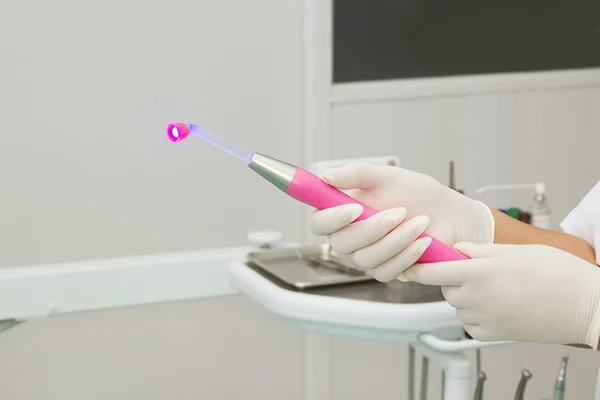 Dentista segurando uma luz UV de cura dentária iluminada na clínica odontológica — Fotografia de Stock