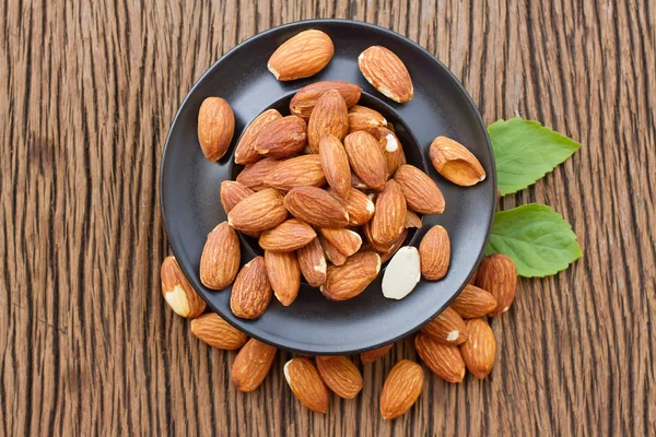 Graine d'amandes en plaquette noire sur fond bois — Photo