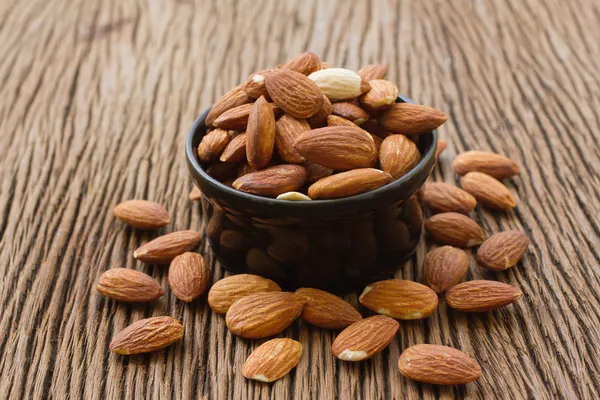 Graine d'amandes dans un bol noir sur fond en bois — Photo