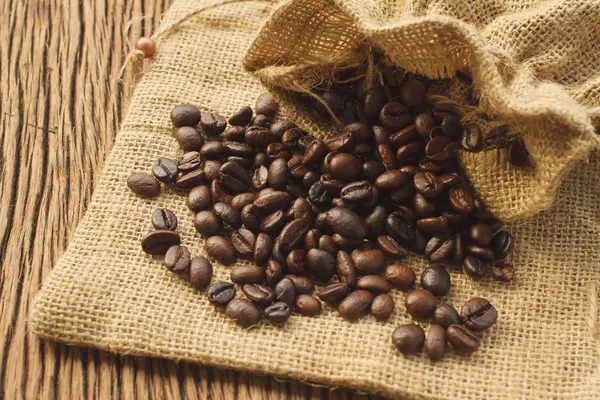 Grãos de café em saco de café em fundo de madeira — Fotografia de Stock