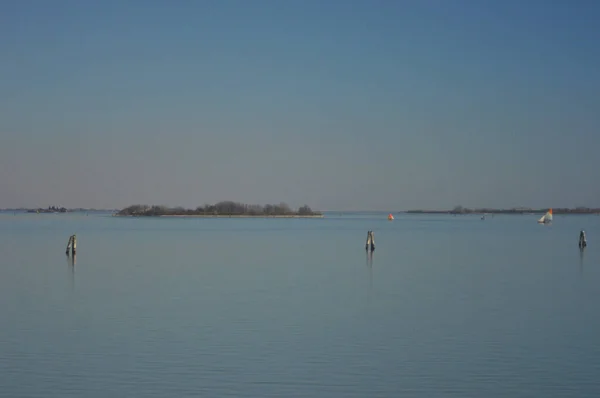 有白色和橙色帆的小帆船停泊在平静的海湾里 海湾里有一些灌木覆盖的岛屿 木制通道标记在前沿阵地上 天空是蓝色的 夕阳的颜色在地平线上 — 图库照片