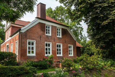 Yeşil ağaçlarla çevrili kırmızı tuğlalardan yapılmış ev.