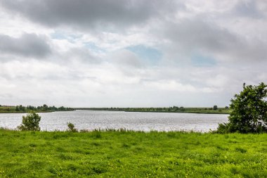 Nehir kenarındaki yeşil düz çayırlar ve bulutlu gökyüzü