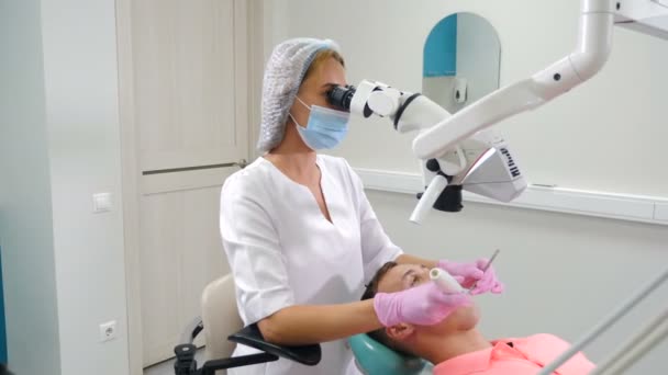 여성 치과의 사는 남성 환자에게 흰색 최장기 현미경을 사용하여 치료 한다. 현대 치과 병원에 장비를 갖추었다. 치아를 복구하고, 하얗게 하고. 검사, 의학, 건강, 기형학. 4k 비디오 — 비디오