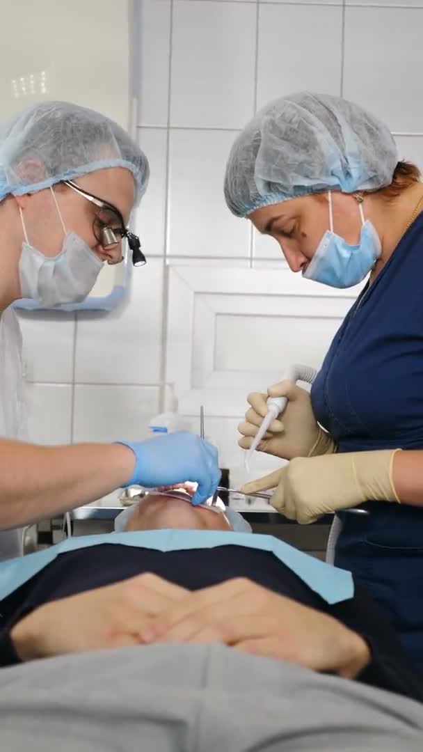 Attente artsen uitvoeren chirurgische operatie installeren van tandheelkundige implantaten of het extraheren van slechte tand. Moderne tandheelkundige kliniek. Verticale video. Professionele tandarts die wortelkanalen behandelt, 4 k video — Stockvideo