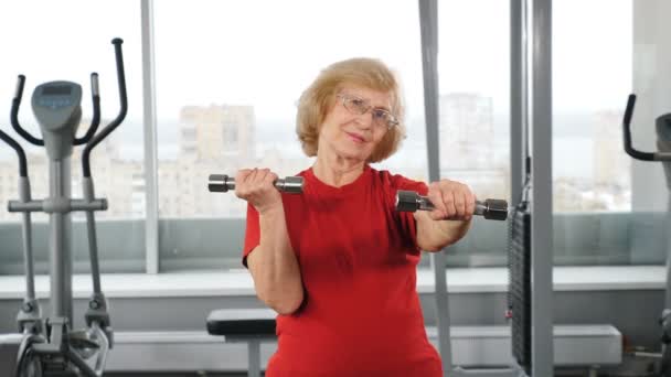 Starsza kobieta ćwiczy podnoszenie ciężarów na hantlach na siłowni. Aktywni emeryci uprawiający sport fitness cardio aerobik, osoby w podeszłym wieku ćwiczące. Zdrowy styl życia. 4 tys. wideo — Wideo stockowe