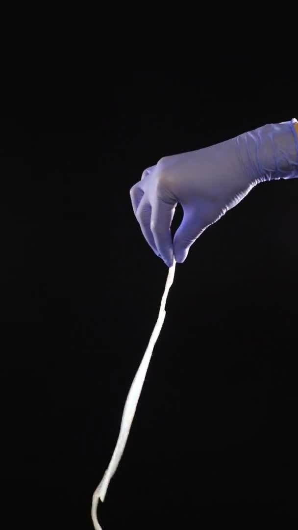 Рука в синей защитной перчатке держит медицинскую маску против вирусов и бактерий на черном фоне, Защита от новой волны коронавируса, COVID-19. Концепция медицины и здравоохранения. Вертикальное видео — стоковое видео