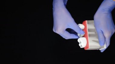 Siyah arka planda insan dişi konsepti. Diş çekilmesi. Mavi eldivenli kadın ellerinin tuttuğu diş modelinde azıdişleri dökülüyor. Dikey görüntü. 4 k video