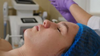 Güzellik uzmanı, kadın müşterinin yüzüne asit soyma çözeltisi sürüyor eldivenli ellerle ovuyor. Cilt bakımı ve sorunlu cilt için prosedürler. Genç bir kadın güzellik kliniğinde yüz bakımı yaptırıyor. 4 bin.