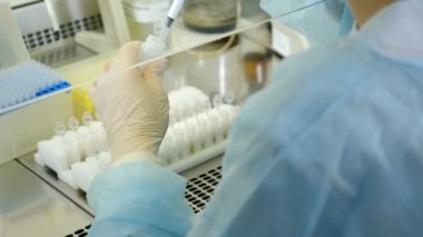 Steril genetik laboratuvarında çalışan bir bilim adamı. Sabahlıklı bir pipetle. Coronavirus analizi. Tıbbi Gelişim Laboratuvarı. Test Tüpü Sıvı ile dolduruluyor, Deney yapılıyor. DNA