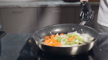 Lokanta mutfağında siyah eldivenli bir şef sebze pişiriyor. Malzemeleri yavaş çekimde fırlatmak ve karıştırmak. Yemek hazırlıyorum. Şef çalışmakla meşgul. Tam Hd