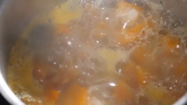 Gotuję danie z dyni. Świeża dynia pokrojona w kostkę w zwolnionym tempie. Proces gotowania zupy z dyni. Składniki do zupy we wrzącej wodzie w rondlu. Widok z góry. Pełny hd — Wideo stockowe