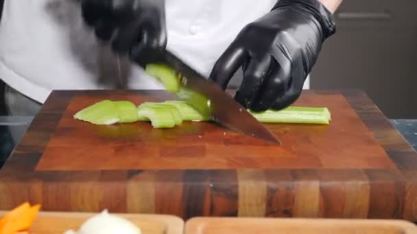 ベジタリアンフードサラダ。黒手袋のシェフは、まな板にセロリをカットします。調理プロセス、クローズアップ。自家製野菜料理。セロリの茎を包丁で細切りにしたものです。フレッシュ — ストック動画