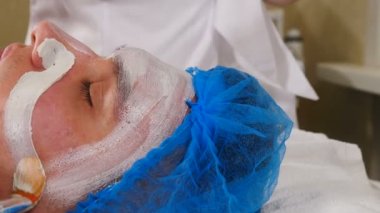 Skin care, dermatology treatment in beauty salon. Beautician applying white moisturizing mask on male face skin. Spa therapy for men getting facial mask. at beauty clinic. 4 k video