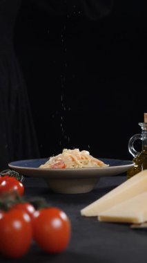 Restoranda siyah arka planda makarna servis ediyorum. Kuru baharatlar taze pişmiş deniz ürünleri makarnasının üzerine düşüyor. Ağır çekim. Dikey görüntü. Lezzetli İtalyan yemekleri. Tam Hd