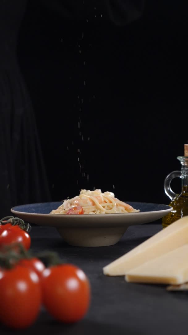 Serveren pasta in restaurant op zwarte achtergrond. Droge specerijen vallen op vers gekookte zeevruchten pasta. Langzame beweging. Verticale beelden. Lekker Italiaans eten. Vol hd — Stockvideo