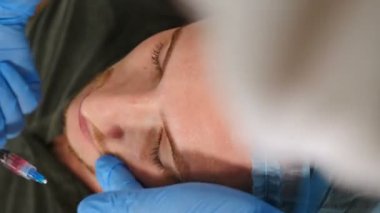 Kozmetik uzmanı, erkek müşterinin yüzüne asit soyarak eldiven takıyor. Cilt bakımı ve sorunlu cilt için prosedürler. Genç adam güzellik kliniğinde yüz bakımı yaptırıyor. Vrtical