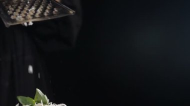 Metal rendeleyici üzerindeki ızgara peynir siyah arka planda izole edilmiş, yavaş çekim. Parmigiano-reggiano peyniri ve çelik rendesi tabağın üzerinde, kapat. Restoran yemeği videosu. Yemek pişirme süreci. Tam Hd