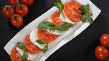 Domatesli mozzarella salatasının üzerine biber döküyorum. Üst Manzara. Yavaş hareket et. Olgun domatesli caprese salatası ve taze yeşil fesleğen yapraklı mozzarella peyniri. Sağlıklı gıda ve vejetaryen konsepti