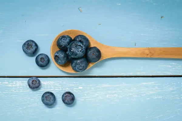 Blaubeeren auf einem Löffel liegend auf blauem Holz Hintergrund — Stockfoto