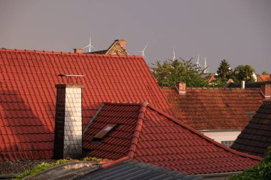 Rüzgar santralinin arka planında bir Alman köyünün kırmızı kiremitli çatıları. Akşam yağmurdan sonraki altın saat.