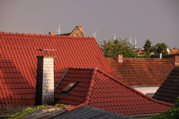 Red tiled roofs of a German village on the wind power station background. Evening golden hour after rain.