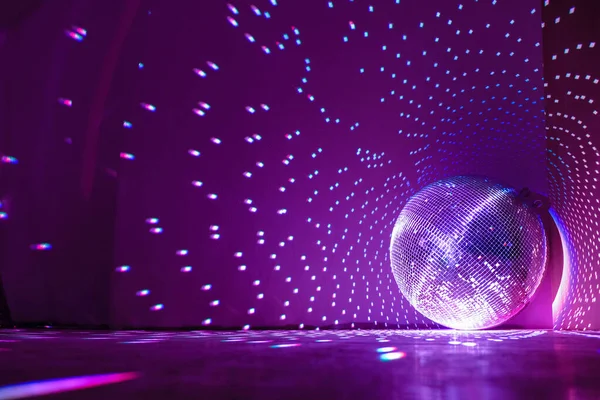 Disco ball reflecting purple light in a dark hall for discos. Holidays concept. Copy space.