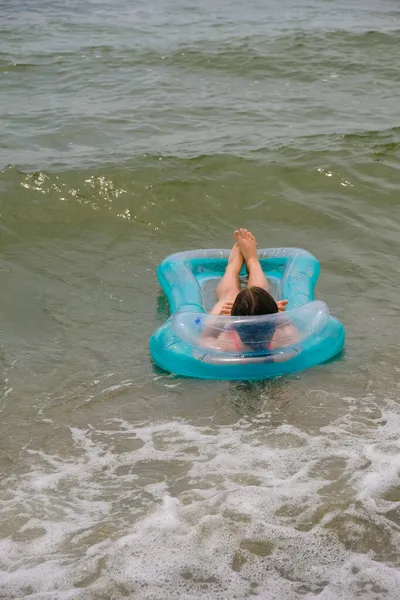海の波の間で膨脹可能なターコイズブルーのマットレスの上の女の子 水の安全コンセプト 垂直画像 — ストック写真