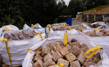 Kahverengi ve bej parke taşları polipropilen büyük çantalarda sarı şerit saplı. Yumuşak kaplarda doğal taş ambalajı.