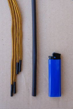 Isı küçültme tüpü, çakmak ve gri kağıt üzerinde sarı ayakkabı bağcıkları. Evdeki pejmürde bağcıkların tamiri. Dikey resim.