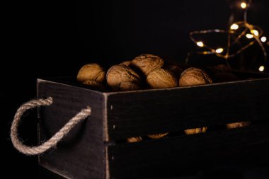 Ahşap bir sandıkta ceviz ve Noel ışıkları arka planında halat sapları. Noel 'den önce oruç tutarken yemek. Siyah fotoğraf.