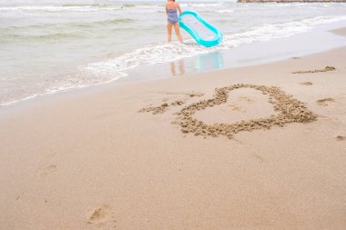 Kumsalda kalbi olan bir deniz plajı. Dalgaların arasında şişme dairesi olan bir çocuk..