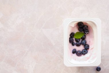 Yoğurda ilave olarak taze yabanmersini. Plastik bardakta standart bir meyve yoğurdu taze yaban mersiniyle kaplıdır. Üst Manzara. Boşluğu kopyala.