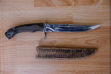 Ahşap bir masanın üzerinde süslü bir bıçak ve kılıç. Av bıçağı. Üst görünüm.