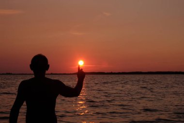 Günbatımı arka planında kollarını kaldırmış mutlu yalnız adam. Kişi güneşi işaret ediyor. Boşluğu kopyala.