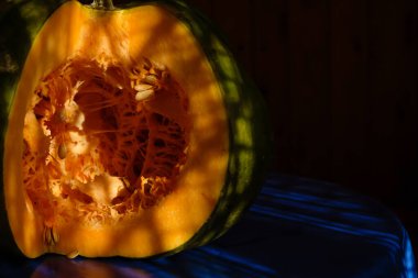 Mutfakta mavi masa örtüsünün üzerinde dilimlenmiş portakal kabağı. Et ve tohum. Sert güneş ışığı. Boşluğu kopyala.