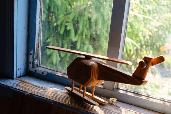 Toy helicopter on the windowsill of an old abandoned house. There is spruce behind the glass. Morning sunlight. Unexpected angle.