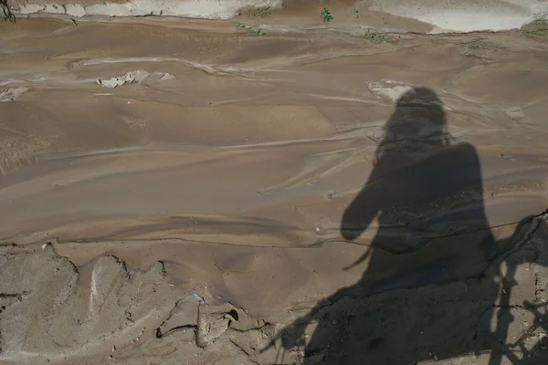 Soil texture after water flow. Clay soil leaching. Shadow of a photographer with a bicycle.