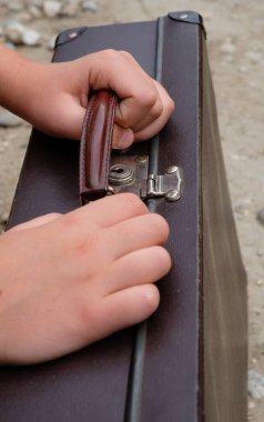 Metal kilidi olan eski kahverengi bavul çocuğun elinde. Endişeli duygu.