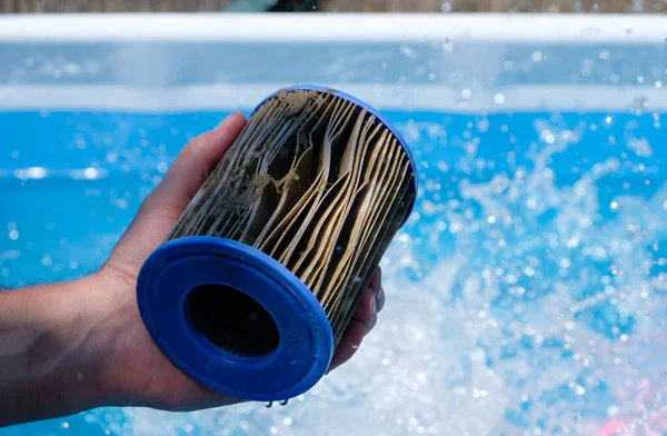 Dirty Replacement Pool Filter Cartridge in a man\'s hand on water splash background. Pool water quality concept. Copy space.