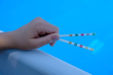 Çocuğun elinde havuz testi şeritleri var. Mavi havuz geçmişi. Su dengesi.