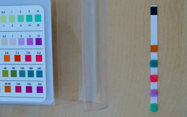 Pool test strip and a comparison chart on a wooden surface. Pool chemistry concept.