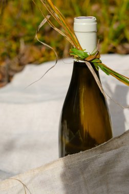 Kenevir masa örtüsünün üzerinde kuru çimenle süslenmiş beyaz şarap şişesi. Güneş ışığı.