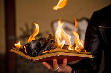 Kağıt kitap yanıp kül olur, beton kiremitler, el yazması yanıklar, insan eliyle açılan bir kitap.