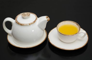 Kalıplı bir çaydanlık ve bir fincan deniz dikenli çay, siyah bir arka planda.