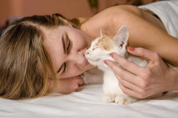 美丽的年轻女子躺在一张白色的床上 与一只生姜猫在一起 拥抱她 爱动物 — 图库照片#