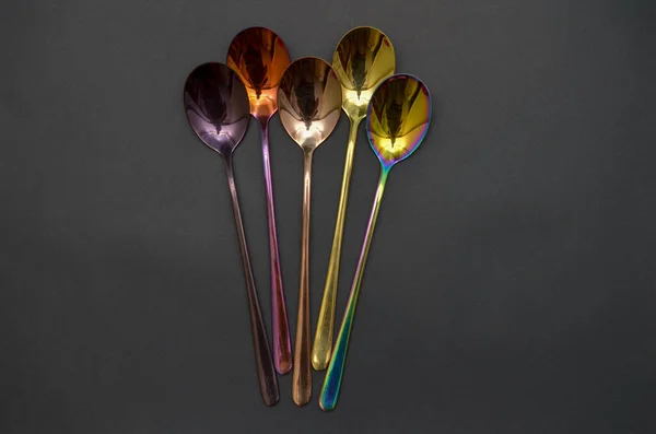 Multicolored table spoons on a plain black background, picture for an article about tableware or cutlery, with a copyspace