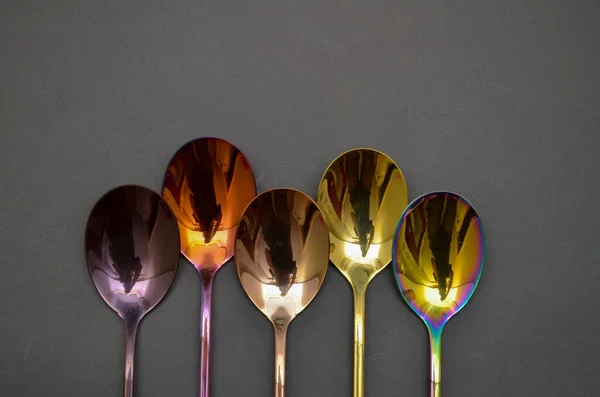 Multicolored table spoons on a plain black background, picture for an article about tableware or cutlery, with a copyspace