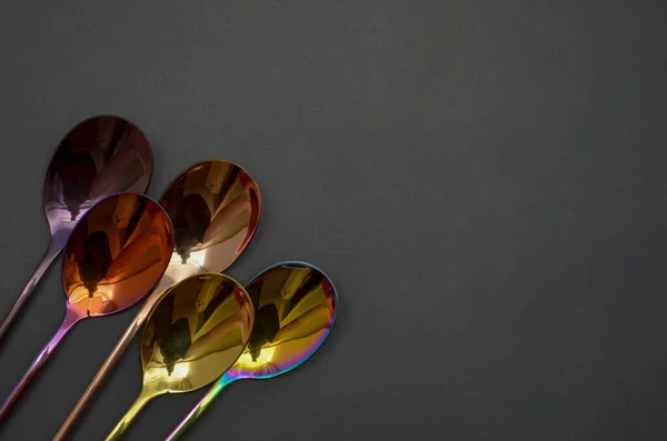 Multicolored table spoons on a plain black background, picture for an article about tableware or cutlery, with a copyspace