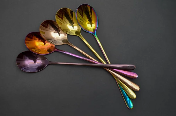 Multicolored table spoons on a plain black background, picture for an article about tableware or cutlery, with a copyspace